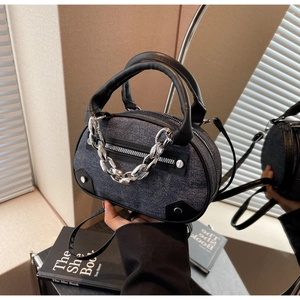 Détail du sac Boston en denim bleu avec chaîne argentée, poignées en cuir et reflet miroir