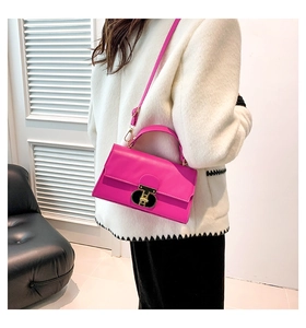 Close-up of hot pink crossbody bag with a gold T-shaped lock on a white jacket