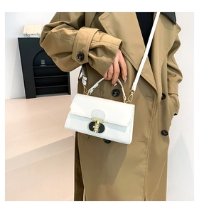 Dettaglio borsa bianca in pelle verniciata con chiusura oro e nera su un trench classico