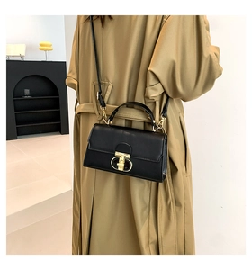 Dettaglio borsa squadrata in pelle nera con fibbia dorata su trench color kaki