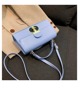 Light blue rectangular shoulder bag with unique gold clasp on a beige blazer background
