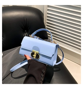 Close-up of light blue flap square bag with golden T-shaped twist lock and top handle
