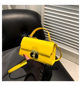 Detail of a bright yellow square handbag featuring a metallic T-shaped decorative clasp