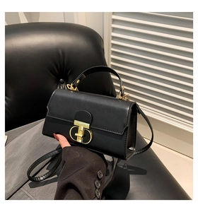 Detail of minimalist black leather crossbody bag with distinctive gold T-bar twist lock