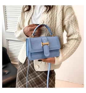 Close-up of light blue crocodile embossed handbag with gold H-buckle and shoulder strap