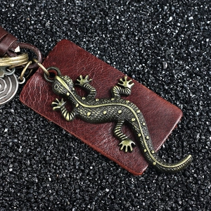 Vintage bronze gecko lizard keychain with leather strap on textured stone background