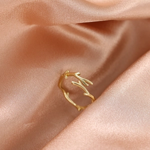 Detailed close-up of golden branch-shaped open ring on soft pink satin fabric background
