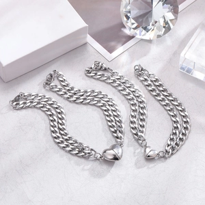 Close-up of silver Cuban link couple bracelets with magnetic heart charm on grey surface