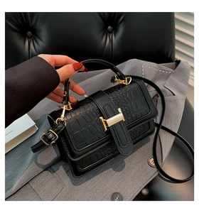 Close-up of black crocodile-embossed leather handbag with elegant gold H-shaped buckle
