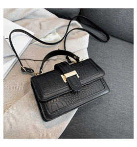 Detail of black faux leather handbag with crocodile pattern and golden metal clasp