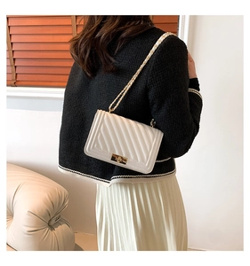 Woman wearing white quilted chain bag with gold hardware in a minimalist interior scene