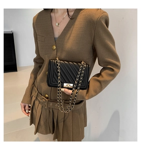 Detail of black quilted chain crossbody bag with gold metallic push-lock on classic suit