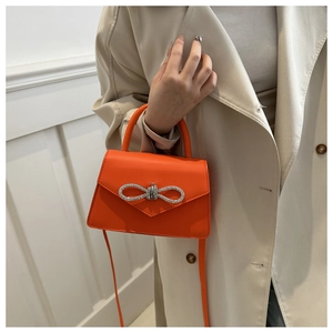 Detail van een feloranje lederen minihandtas met een glinsterende strass-strikgesp