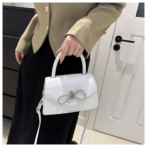 Detail van witte lederen handtas met glanzende strass-strik en rond handvat