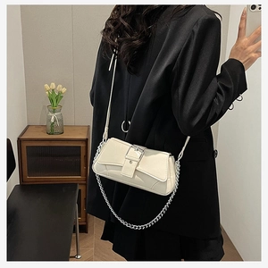 Detail of a creamy white glossy shoulder bag with a silver buckle and chain strap