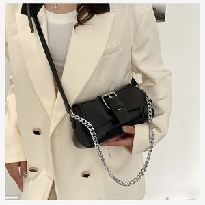 Detail of black leather shoulder bag with silver buckle and chain strap on a model