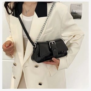 Detail of a black patent leather baguette bag with silver chain strap and metal buckle