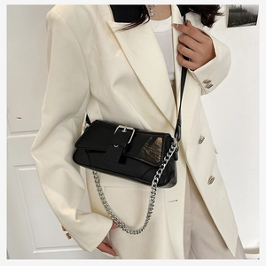 Detail of black glossy faux leather baguette bag with large buckle and silver chain strap