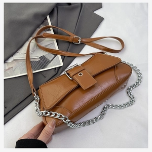 Detail of caramel brown textured leather handbag with silver buckle and chain strap