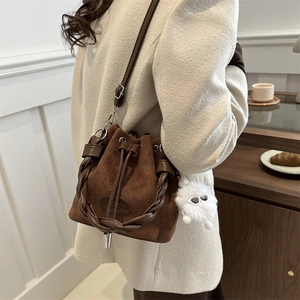 Dark brown drawstring bucket bag with woven handle and plush charm on a beige coat