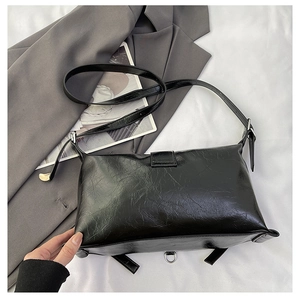 Detail of black rectangular shoulder bag with oily leather texture and adjustable strap