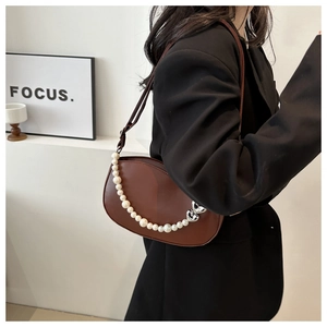 Detail of a brown leather half-moon bag with pearl chain and silver heart buckle