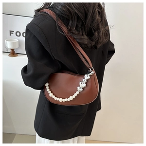 Close-up of brown crescent bag featuring pearl chain and silver heart charms detail