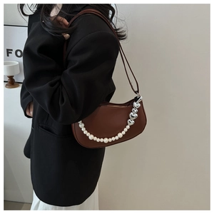 Detail of brown half-moon bag featuring pearl and silver heart chain on a model