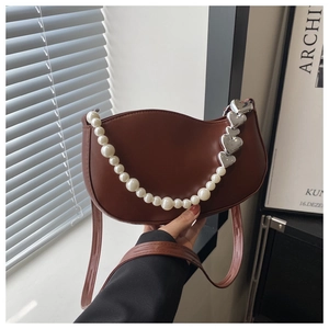 Detailed shot of brown crescent bag with white pearls and silver heart chain accessories