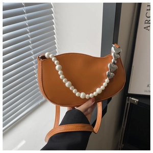 Detail of bright orange crescent bag with pearl strap and silver heart charms