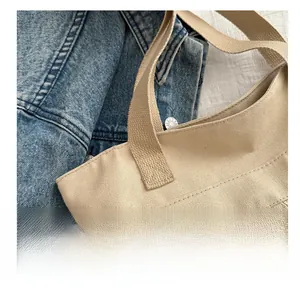 Détail du sac cabas en toile beige avec coutures renforcées et poche zippée en métal