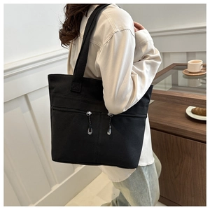Détail du sac cabas en toile noire montrant deux poches zippées et la texture du tissu