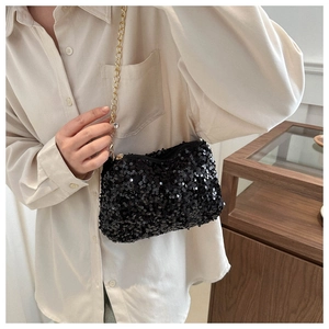 Detail of black sequin shoulder bag featuring a gold chain strap on a model shoulder