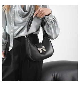 Gros plan du sac hobo noir avec nœud argenté porté par un mannequin dans un style chic
