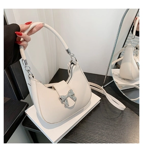 Détail d'un sac demi-lune blanc cassé avec nœud argenté posé sur un bureau élégant