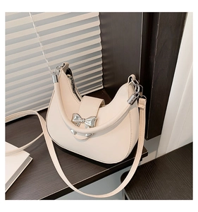 Détail d'un sac demi-lune crème avec un nœud en métal argenté et texture en cuir