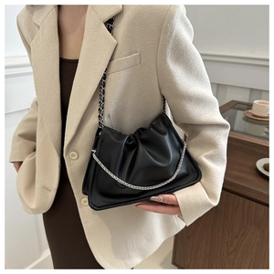 Close-up of black pleated cloud bag with silver metal chain on a model in a beige blazer