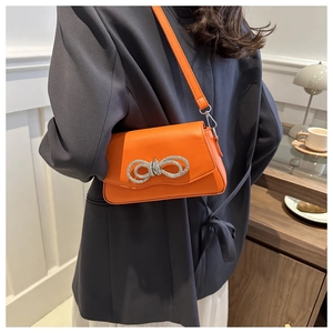 Détail d'un sac bandoulière orange en cuir avec boucle nœud en strass étincelants