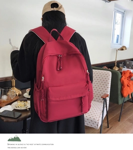Detailed view of red nylon backpack featuring braided zipper pulls and side pockets