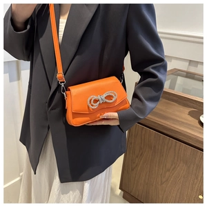 Sac bandoulière orange porté à l'épaule avec une boucle nœud en strass étincelante