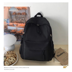 Detail of minimalist black nylon backpack featuring woven zipper pulls and side pockets