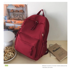 Detail of red travel backpack featuring woven rope zipper pulls and large front pocket