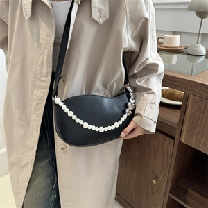 Chic black crescent shoulder bag with elegant pearl chain and heart charms on a model