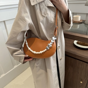 Orange faux leather half-moon bag with pearl chain and heart charm over a trench coat