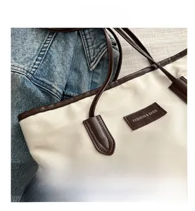 Detail of minimalist cream tote bag with brown leather handles and brand logo patch