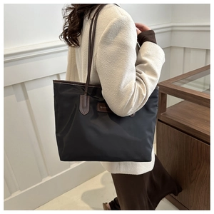 Detail of minimalist black nylon tote bag with brown leather straps and fashion label