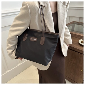 Close-up of black nylon tote bag with brown leather handles worn by a female model
