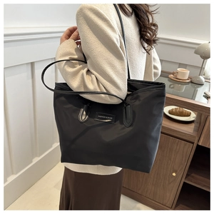 Minimalist black nylon tote bag with fashion label shown in a cozy home setting
