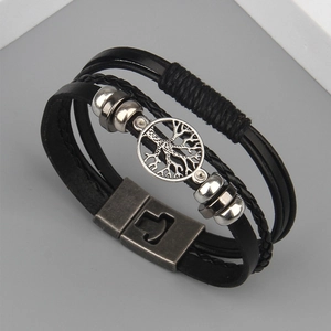 Close-up of tree of life metal charm and multi-layer braided leather wristband