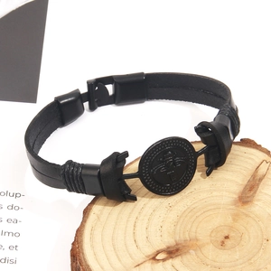 Gros plan du bracelet en cuir noir avec écusson d'épée ailée sur un support en bois